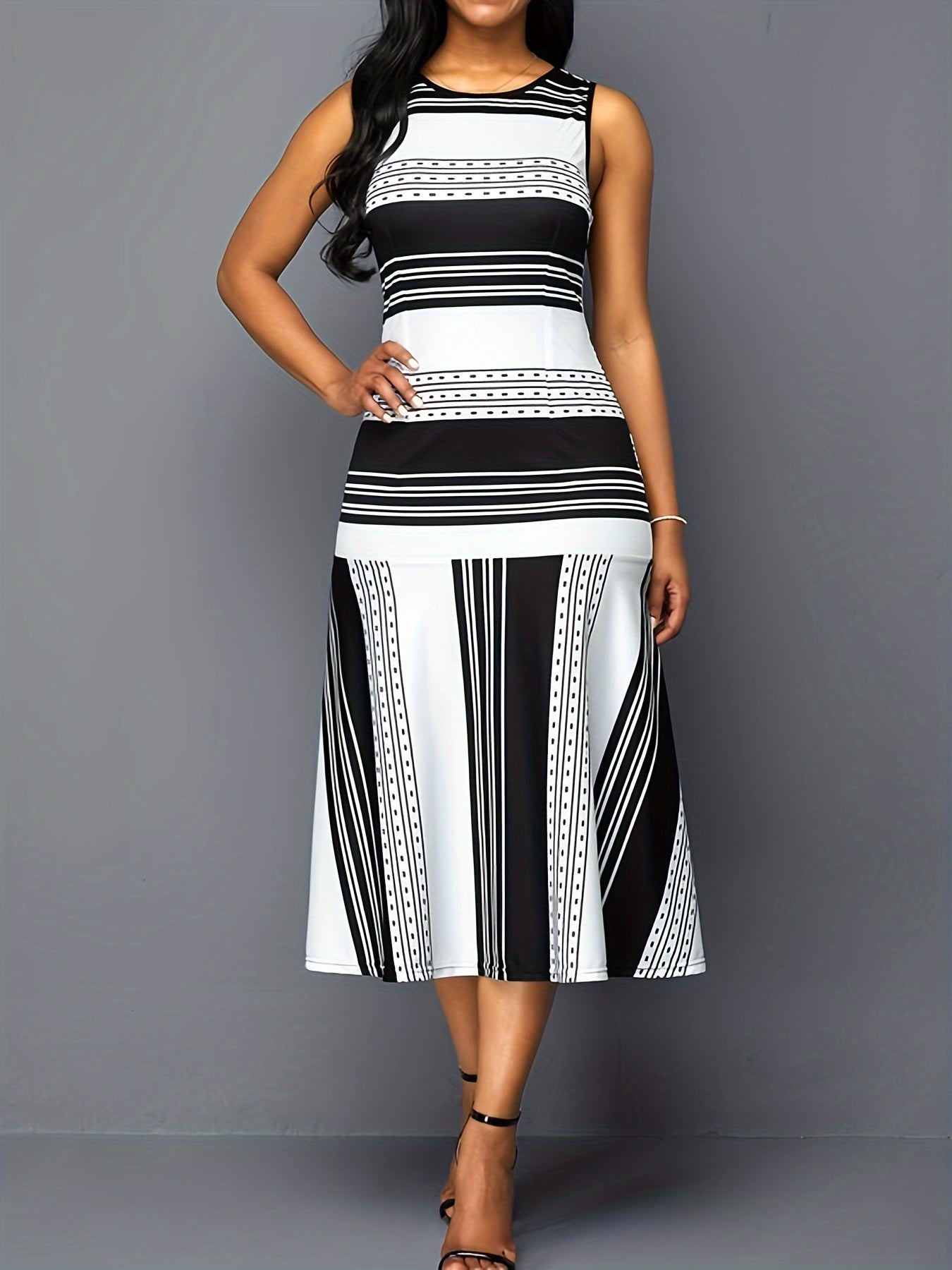 A woman wears a sleeveless, crew-neck midi dress featuring a black and white striped pattern.