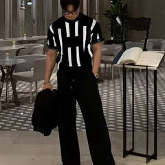 A man wears a black short-sleeve knitted crew neck sweater featuring a white vertical stripe pattern.