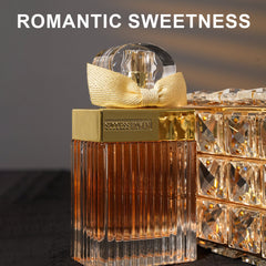 A rectangular glass perfume bottle with a gold cap and a decorative gold ribbon bow.