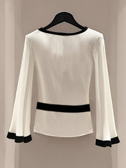 A white long-sleeve blouse with a round neck, black trim, and flared cuffs.