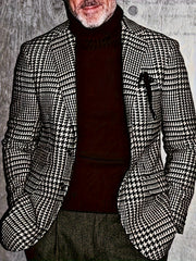 A man wears a black and white houndstooth blazer over a dark brown turtleneck sweater.
