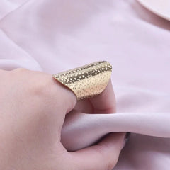 A wide, gold-toned stainless steel ring with a textured, hammered finish worn on a finger.