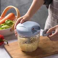 A person uses a manual pull-string vegetable chopper to mince garlic on a wooden cutting board.
