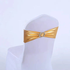 A metallic gold spandex chair sash with a decorative rhinestone buckle wrapped around a white chair.