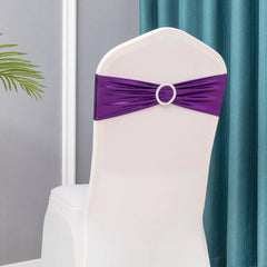 A purple metallic spandex chair sash with a decorative rhinestone buckle on a white chair cover.