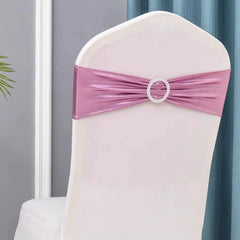 A metallic pink spandex chair sash featuring a decorative circular rhinestone buckle.