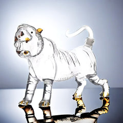 A clear glass tiger-shaped decanter with metallic accents standing on a reflective surface.