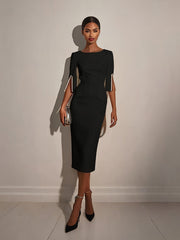 A woman wears a black midi-length bodycon dress with half sleeves featuring pearl-trimmed slits.
