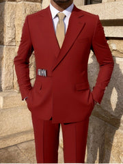 A man wears a solid red double-breasted suit with a metal belt detail and a beige tie.