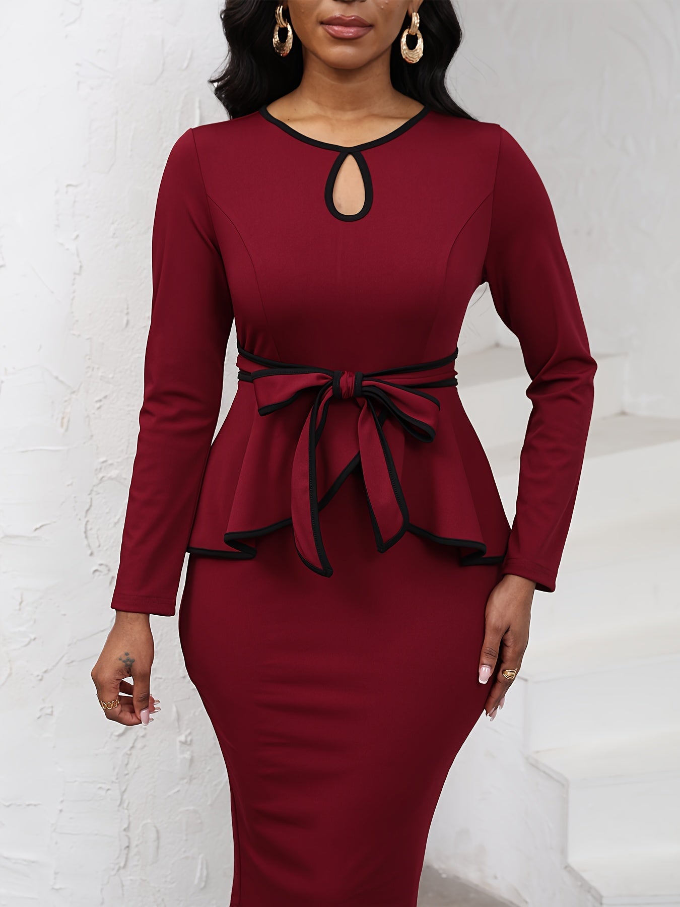 A long-sleeve burgundy midi dress with a black contrast trim, keyhole neckline, and waist tie.