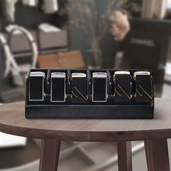 A black leather organizer box holding six belts with visible buckles on a wooden table.