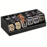 A black leather organizer box containing six rolled belts with various buckle styles.