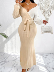 A woman wears a long-sleeved, two-tone beige and white wrap dress with a cinched waist.