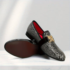 A pair of black and silver floral pattern loafers featuring a prominent gold buckle and red lining.