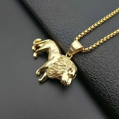 A gold-plated stainless steel lion pendant necklace resting on a black textured surface.