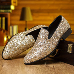 A pair of gold glitter slip-on loafers with a pointed toe resting on a wooden surface.