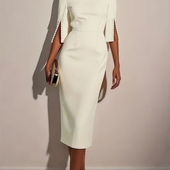 A woman wears an elegant white knee-length pencil dress with split sleeves and pearl detailing.