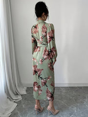 A woman wears a sage green midi dress with a pink floral print, long lantern sleeves, and a waist tie.