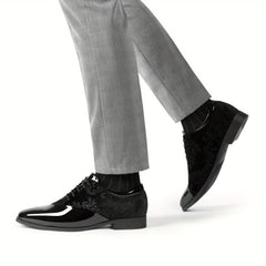 A pair of black velvet and glossy patent leather lace-up oxford dress shoes worn with grey trousers.