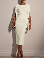 A woman wears an elegant white knee-length pencil dress with split sleeves detailed with pearls.