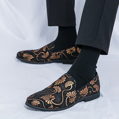 Men's black slip-on shoes featuring a gold floral embroidery pattern and a rubber sole.