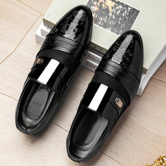 A pair of black slip-on dress shoes featuring an embossed toe, mesh panel, and metallic detail.