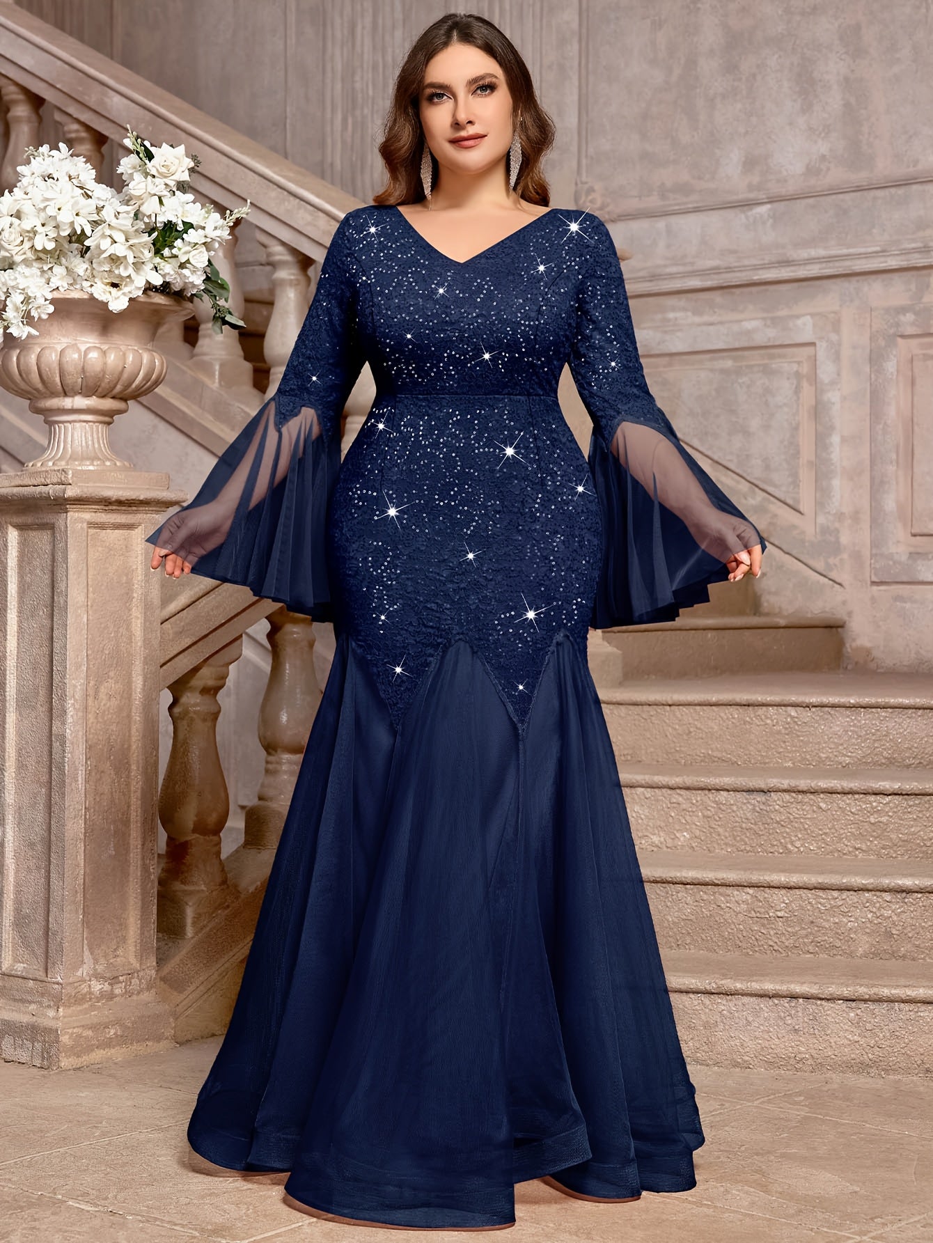 A navy blue plus-size mermaid gown featuring a sequined lace bodice, V-neck, and bell sleeves.