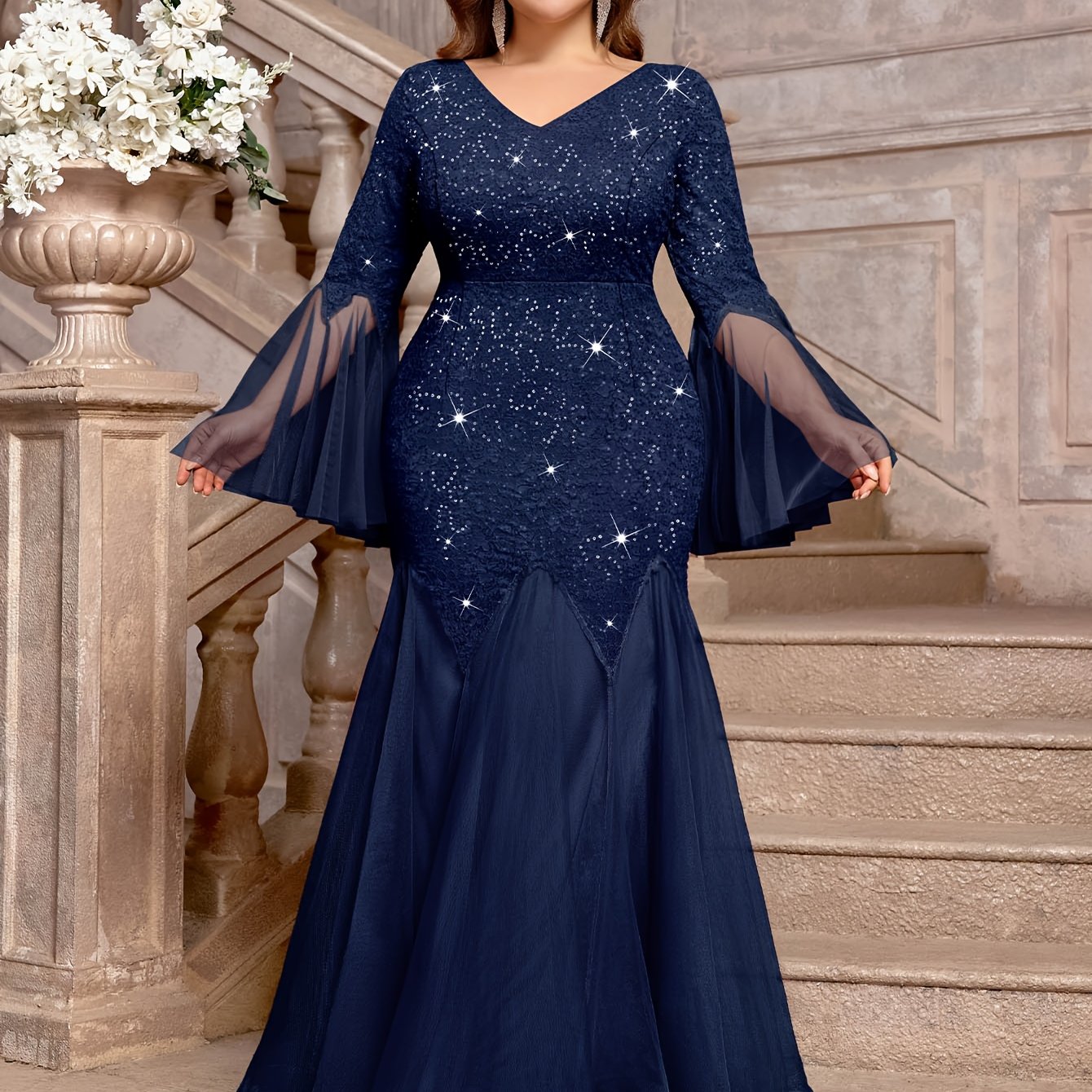 A navy blue plus size mermaid gown featuring sequin lace, a V-neck, and sheer bell sleeves.
