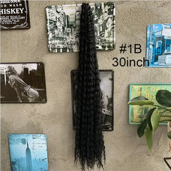 A long, black, deep-wave crochet hair extension hangs against a wall decorated with vintage signs.