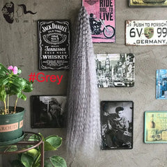 A long, grey, deep wave crochet hair extension hangs against a wall decorated with vintage signs.