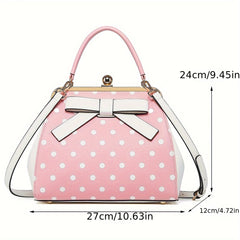 A pink and white polka dot handbag with a bow, kiss lock closure, and removable shoulder strap.
