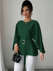 A woman wears a dark green long-sleeve blouse with a crew neck and a matching belted waist.