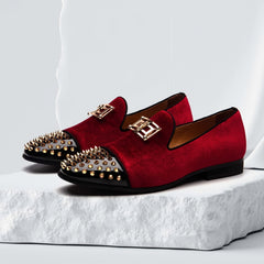 A pair of red velvet loafers with black patent leather toe caps, gold spikes, and gold hardware.