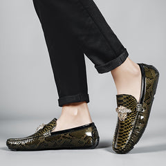 Men's slip-on loafers featuring a metallic snake-skin pattern and a decorative gold emblem.