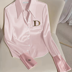 A light pink long-sleeved formal shirt with a wide collar and a prominent gold D logo on the chest.