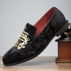 A black velvet slip-on loafer with gold embroidery resting on a wooden surface.