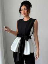 A sleeveless black and white peplum blouse featuring a round neck and a large front bow tie.