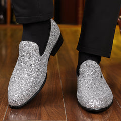A pair of men's silver glitter slip-on formal shoes with a pointed toe and black rubber soles.