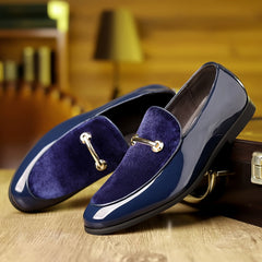 A pair of navy blue slip-on loafers featuring a velvet panel and a gold-tone metal bit detail.