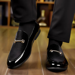 A pair of black slip-on loafers featuring a velvet-textured vamp and a gold-tone metal bar detail.