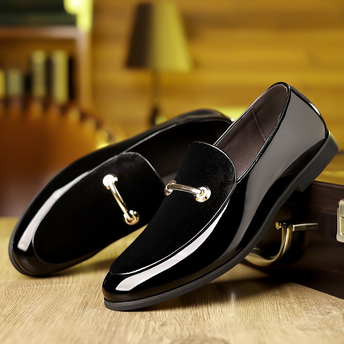 A pair of black slip-on loafers featuring a glossy finish, a suede-like vamp, and gold-tone hardware.