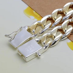 Close-up of the 925 Sterling Silver Solid 10mm Chain Bracelet for men and women, featuring silver and gold links with a visible 925 stamp, displayed on a pale surface with yellow accents and brown paper.