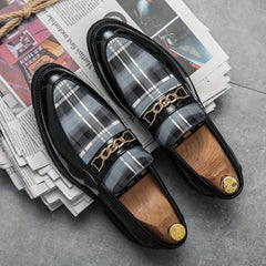 Men's black plaid slip-on loafers featuring a pointed toe and a decorative gold-tone chain detail.