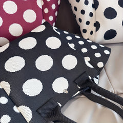 A black and white polka dot knit tote bag with a magnetic closure and fixed shoulder straps.