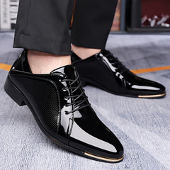 A pair of black patent leather dress shoes with a pointed toe and gold-tone metal tip detail.