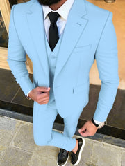 A man wears a light blue three-piece suit with a white shirt, black tie, and black loafers.