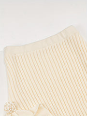 A cream-colored, high-waisted, ribbed knit skirt featuring a delicate rose applique detail.