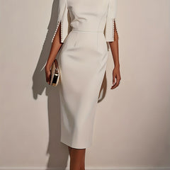 A woman wears an elegant white knee-length pencil dress with split sleeves detailed with pearls.