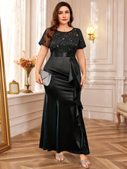 A plus size black floor-length dress with a sequined lace bodice and a ruffled mermaid hem.