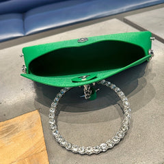 A dark green faux leather clutch with a circular rhinestone-embellished handle.